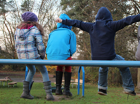 Drei Kinder sitzen mit dem Rücken zum Betrachter auf einer blauen Stange.