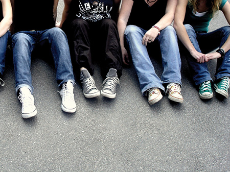 Jugendliche sitzen in Jeans und Turnschuhen auf Asphalt in einer Reihe.